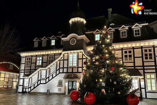 Das Foto zeigt das Historische Rathaus von außen. Es ist dunkel, das Gebäude wird aber von Licht angestrahlt, auch in den Fenstern ist Licht. Vor dem Gebäude steht eine etwa sieben Meter hohe geschmückte Tanne. Große Christbaumkugeln in Rot liegen vor dem Baum auf dem Boden.