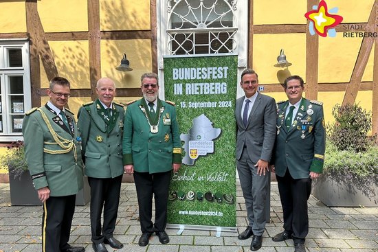 Die in der Bildzeile genannten Personen stehen vor dem Alten Progymnasium. Die Hausfassade besteht aus Fachwerk. Die Vertreter der Schützen tragen Uniformen. Alle Personen schauen in die Kamera.