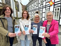 Katrin Dechange, Swetlana Reimer sowie Brigitte Schick und Christa Peitz steheh nebeneinander vor dem historischen Rathaus und halten je einen Flyer in Richtung der Kamera.