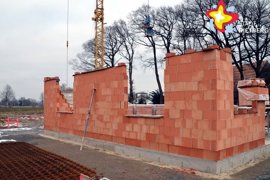 Das Bild zeigt den begonnen Rohbau eines Hauses mit roten Steinen vor grauem Himmel.