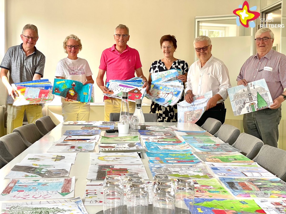 Heinrich Rasche, Anja Rodenbeck, Norbert Laumeier, Doris Vogel, Bertwald Adrian und Otto Hartmann stehen nebeneinander mit von Kindern gemalten Bildern in den Händen. Auf dem Tisch vor ihnen liegen ordentlich nebeneinander zahlreiche weitere solcher Kinderbilder.